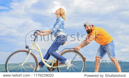 girl cycling while boyfriend support her.