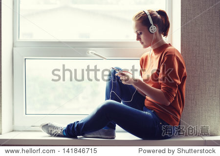girl sits on window sill and listens to music