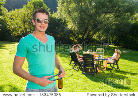 portrait of handsome man holding tongs and wine bottle at garden