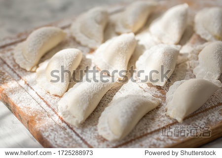 Raw dumplings on a wooden board on grey table in the morning sun. The process of making dumplings. Traditional homemade food. Slavic traditional dish. Dough for dumplings. Close up. Top view