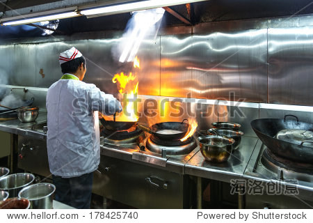 chef in restaurant kitchen at stove with pan doing flambe on