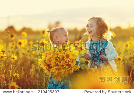 two cute little laughing girls in the field of sunflowers
