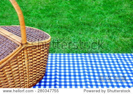 picnic basket on the table with blue white checkered tablecloth.