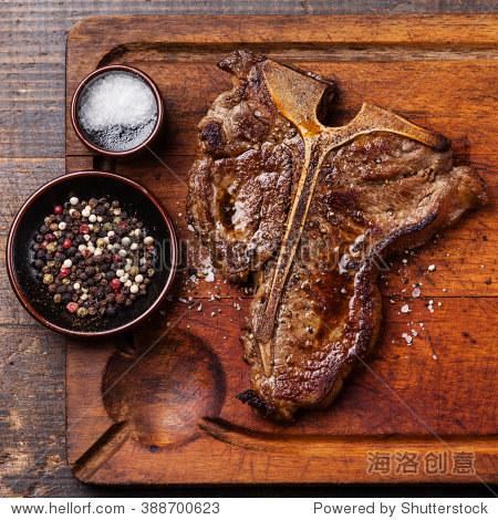 grilled t-bone steak with salt and pepper on cutting board on