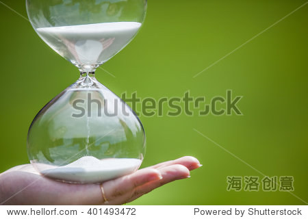 hand holds an hourglass on green background.