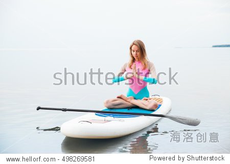 young woman doing yoga on sup board with paddle.