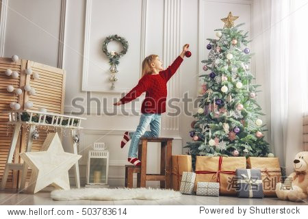 Merry Christmas and Happy Holidays! Cute little child girl is decorating the Christmas tree indoors.