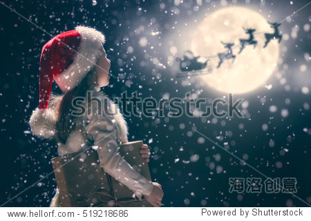 Merry Christmas and happy holidays! Cute little child girl with xmas present. Santa Claus flying in his sleigh against moon sky. Kid enjoy the holiday. Portrait kid with gift on dark background.