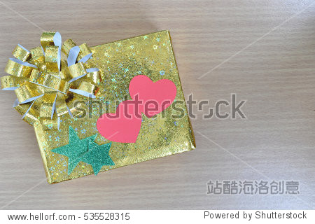 gold gift box with red paper heart shape and green star on wood