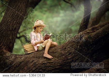 A pretty little blonde girl in a straw hat reading a book on a large spreading tree. Children and science.