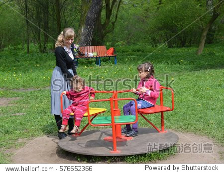 the young woman rolls two children on a roundabout in the park