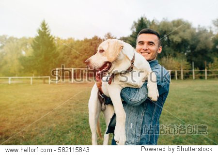 smiling man holding his dog labrador in hands in park