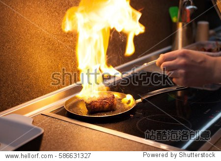 chef cook in kitchen with pan over stove doing flambe.