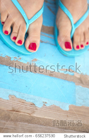 lady"s feet with red nail varnish in sandals on the sandy beach