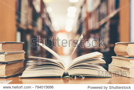 Education learning concept with opening book or textbook in old library stack piles of literature text academic archive on reading desk and aisle of bookshelves in school study class room background