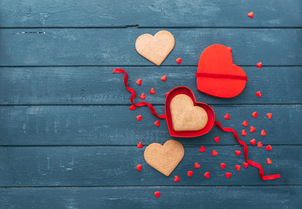open heart shape gift box with cookies over wooden background.