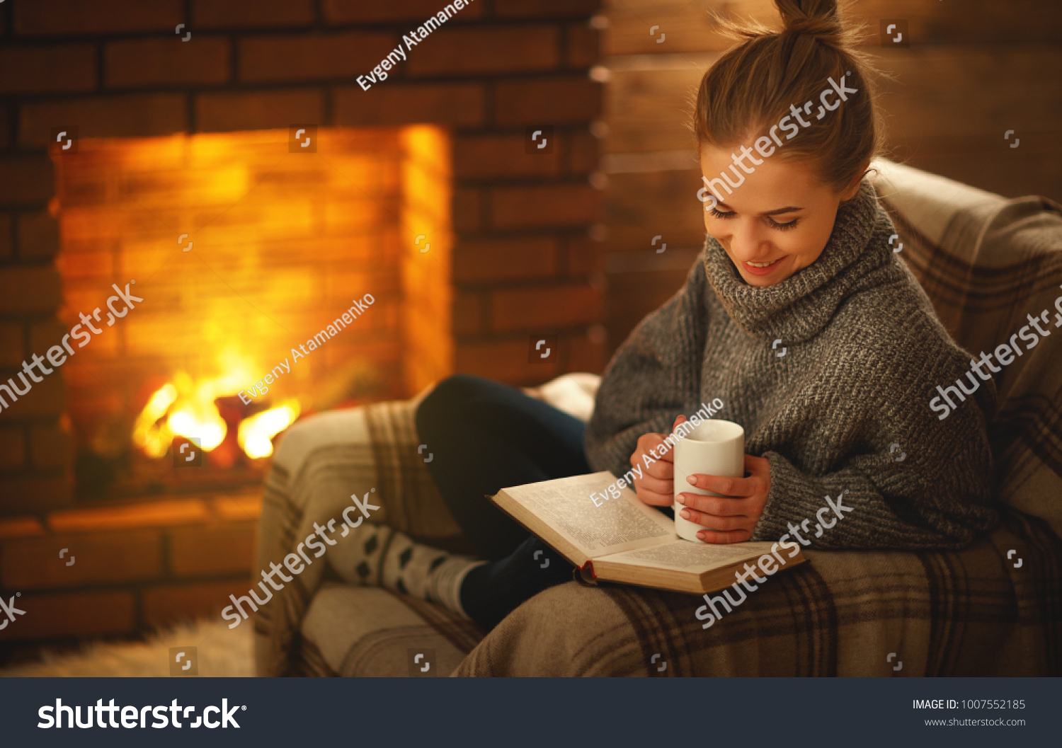 young woman enjoys reading a book by the fireplace on a winter evening