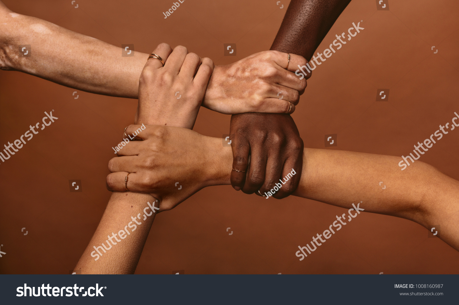 Four diverse women holding each others wrists in a circle. Top view of female hands linked in the lock against brown background.