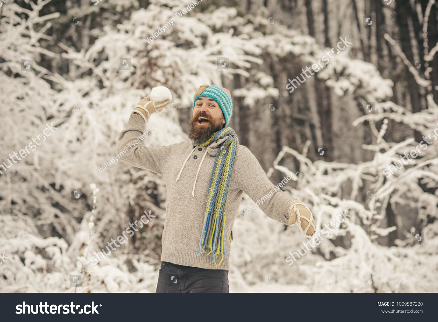 Snow fight  sport  rest. Bearded man smile with snowballs in snowy forest. Temperature  freezing  cold snap. Skincare  beard care in winter. Hipster in thermal jacket  hat  scarf  beard warm in winter