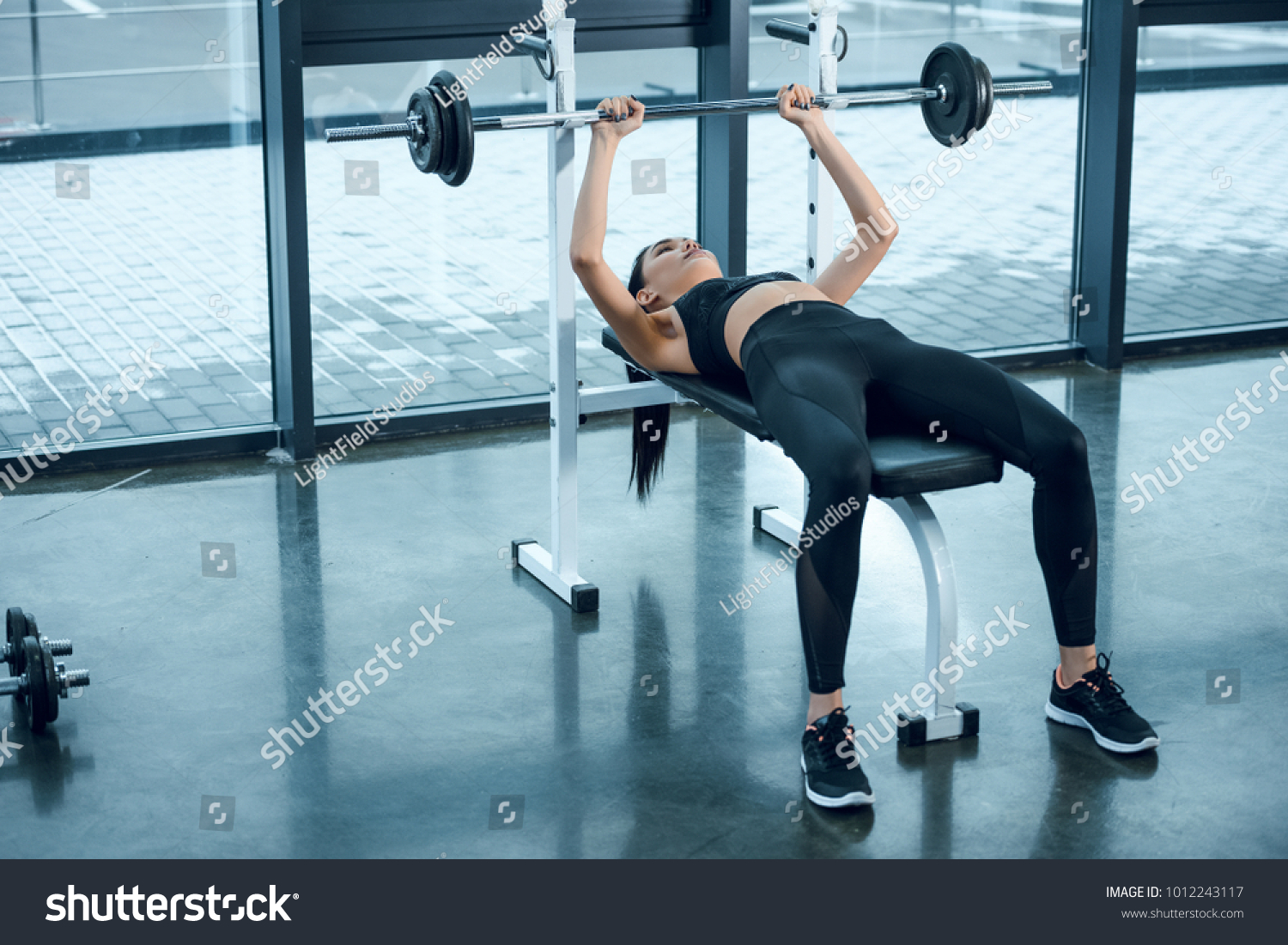 young athletic woman lifting barbell while lying on bench at gym