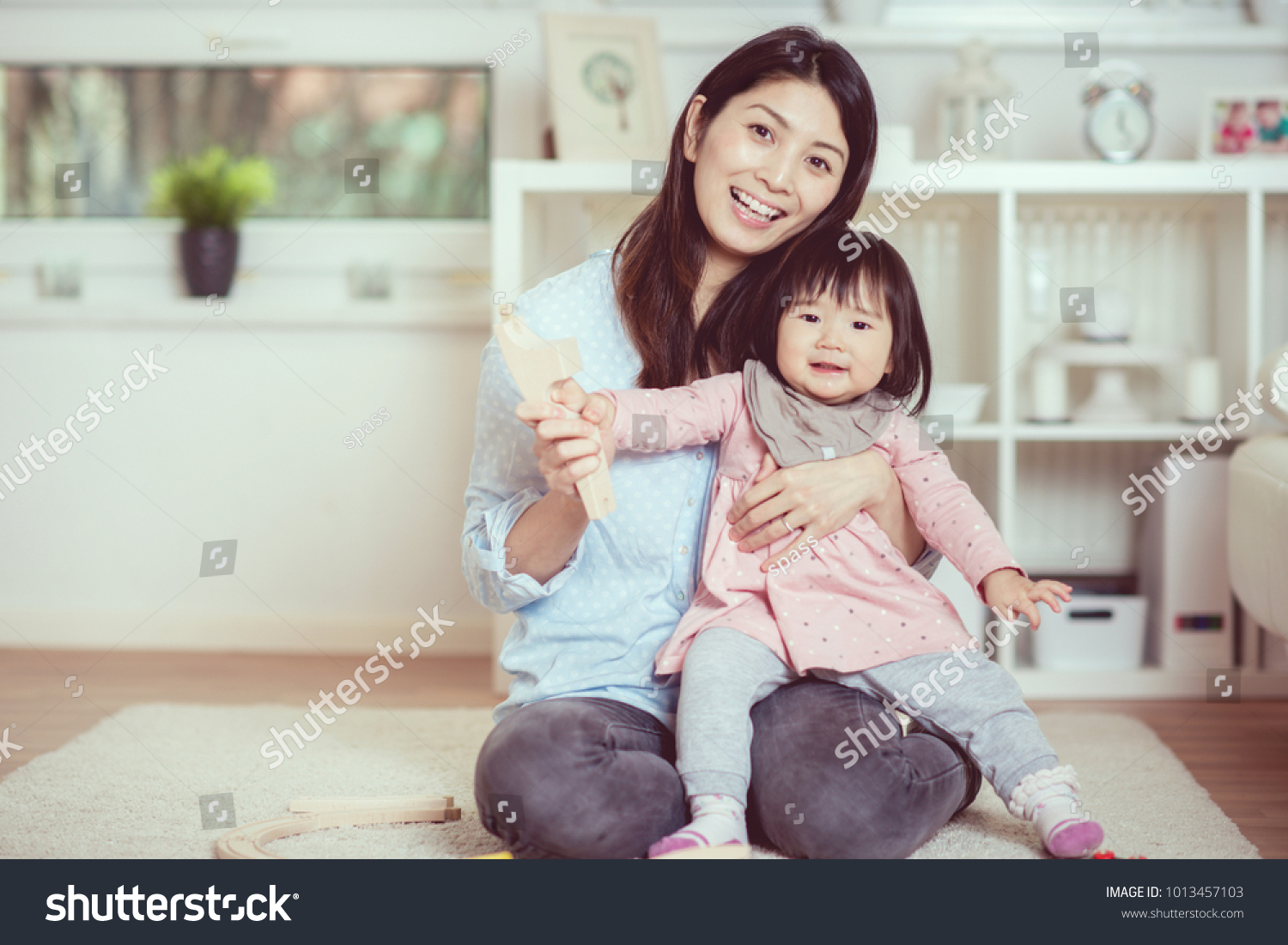 Pretty japanese woman playing with her cute laughing baby girl on the floor at home