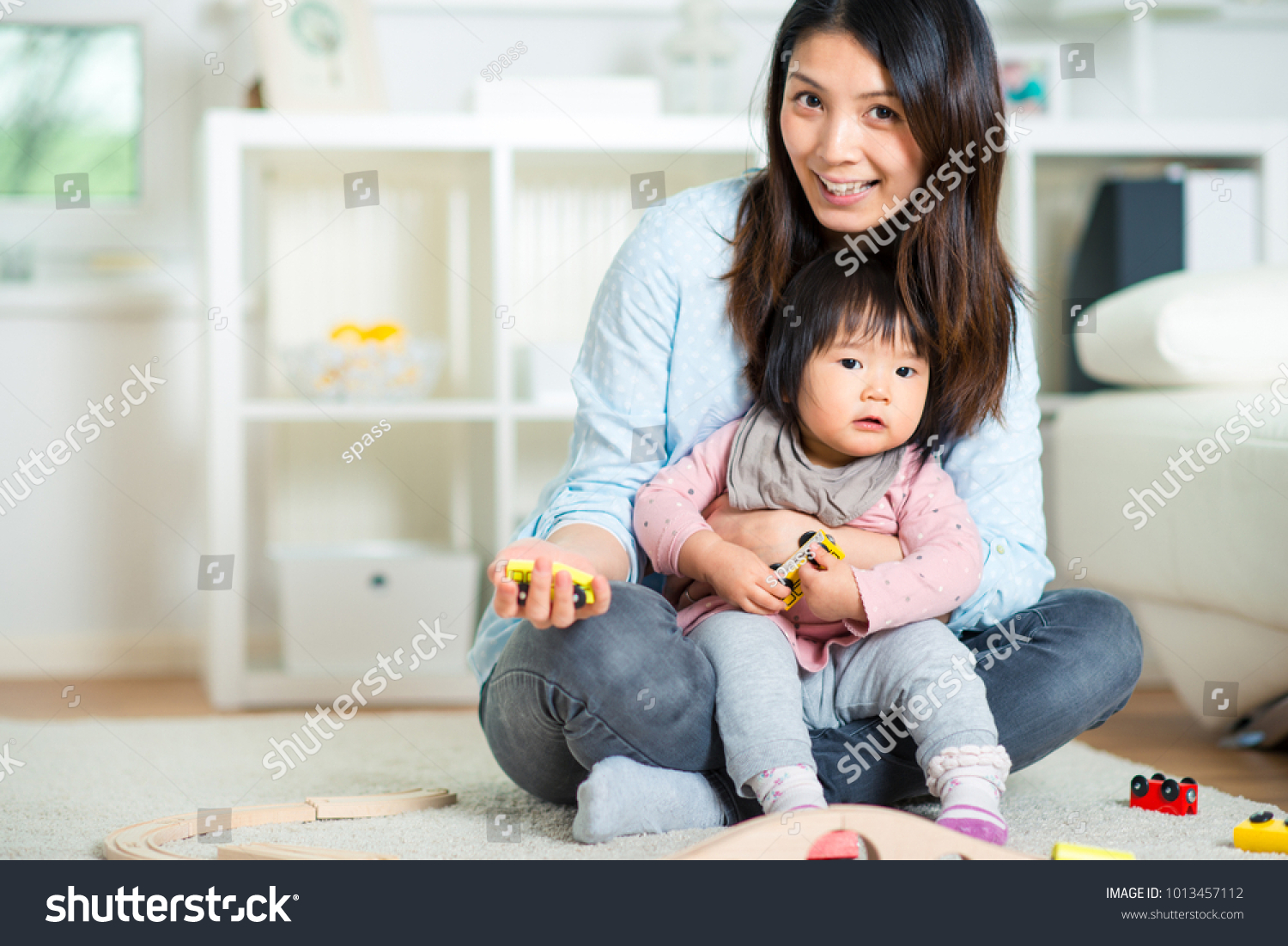 Pretty japanese woman playing with her cute laughing baby girl on the floor at home