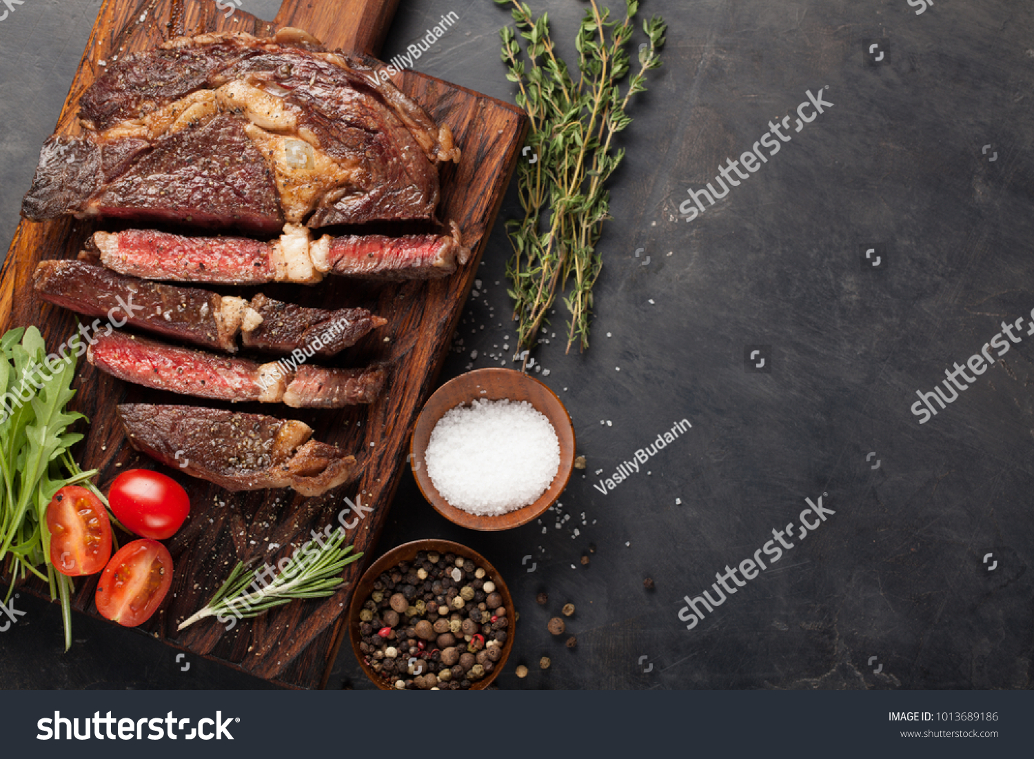 Grilled ribeye beef steak with red wine herbs and spices on a dark stone background. Top view with copy space for your text