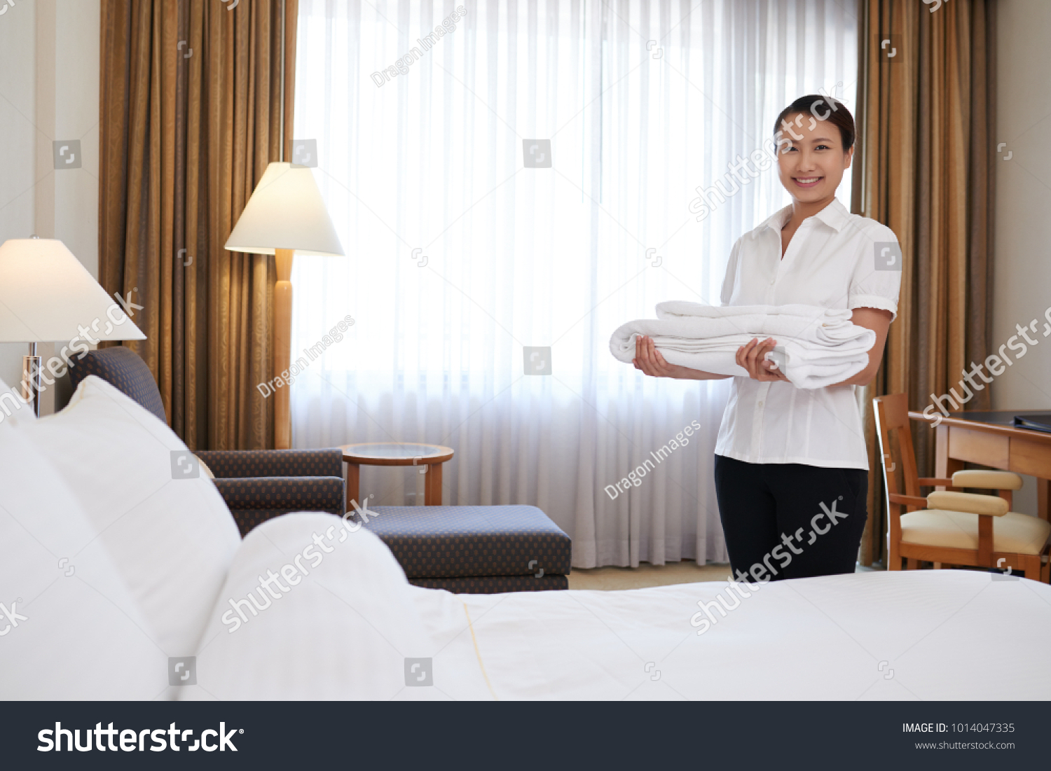 Happy young Asian chambermaid with a stack of fresh towels