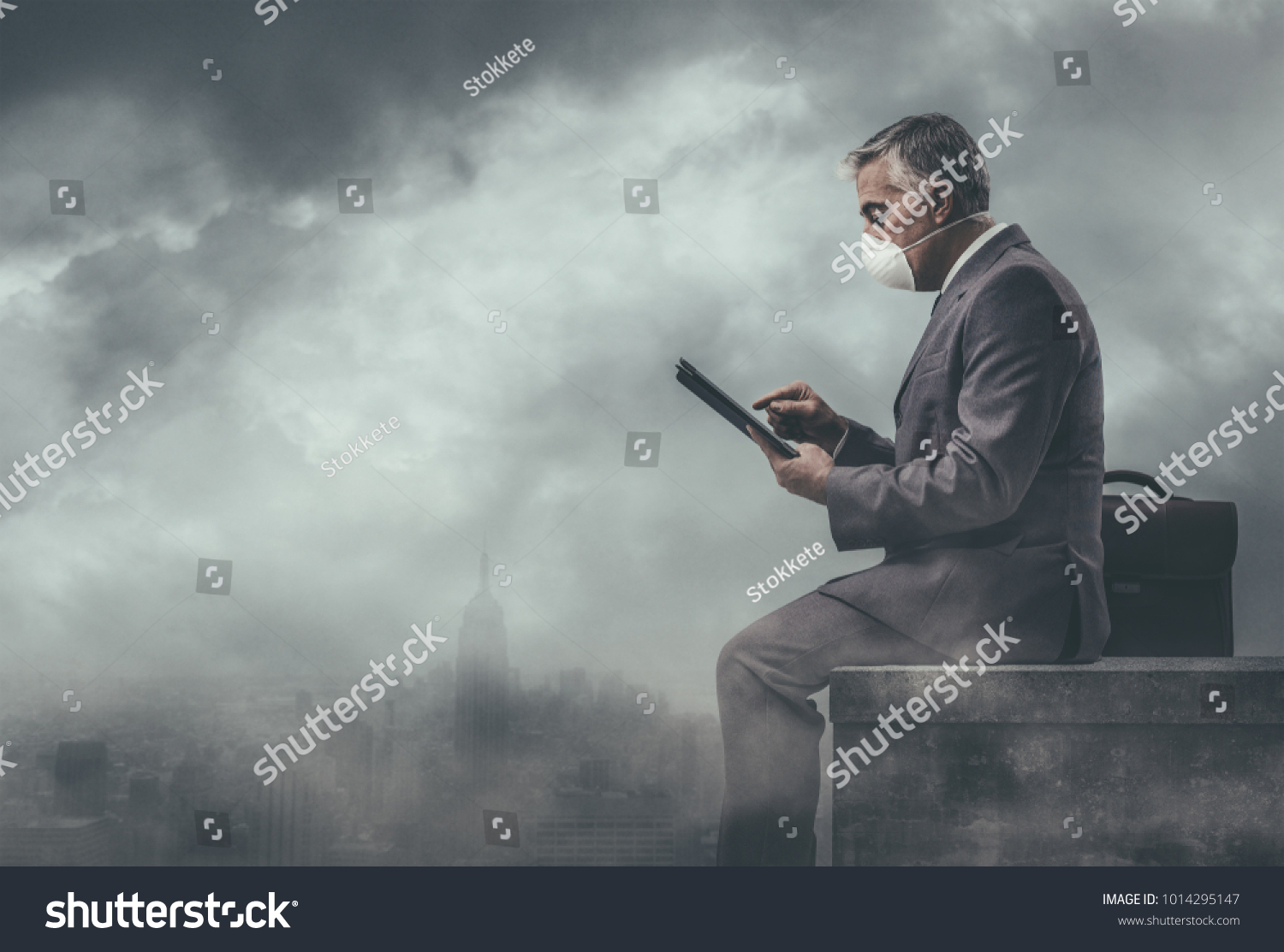 Businessman sitting on a rooftop in a polluted city and using a tablet: environmental pollution and business concept