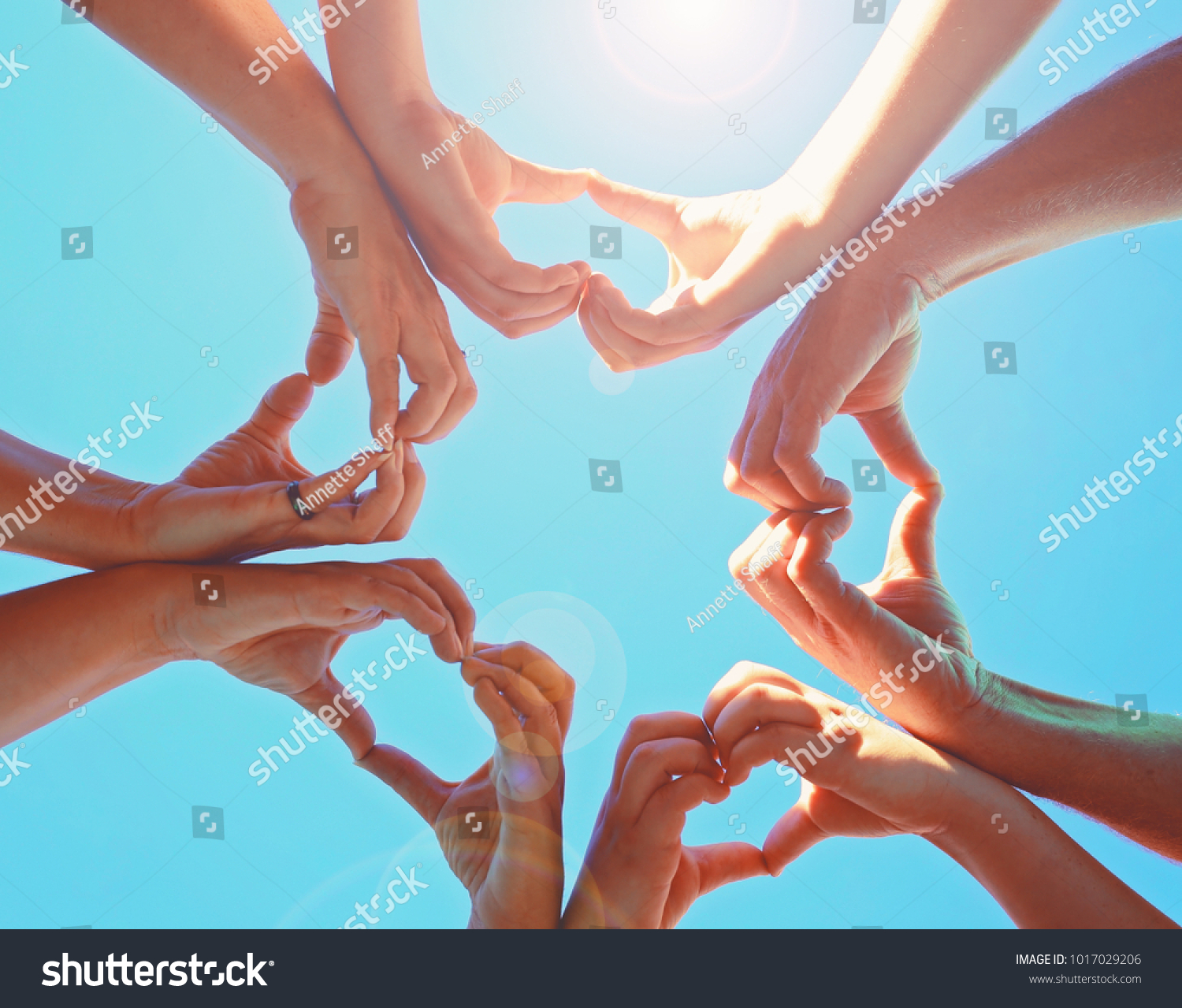 overhead view of a group of people making heart shapes with their hands directly below the sun with a lens flare toned with a retro vintage instagram filter