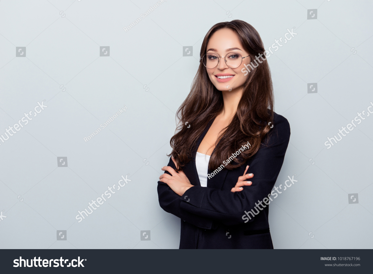 Portrait with copy space of young caucasian stunning nice cheerful headmistress in black jacket formal wear with crossed arms and beaming smile standing over grey background