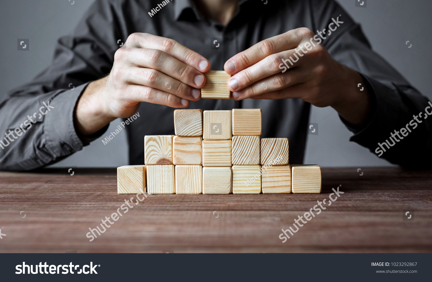 Businessman building a pyramid of wood blocks. Concept of business hierarchy and business strategy.
