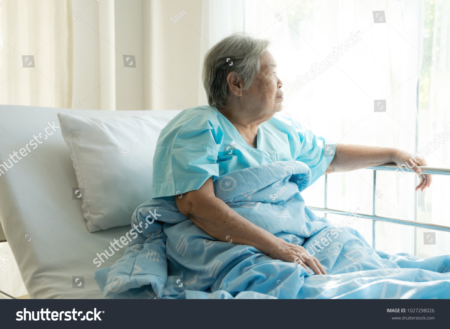 Elderly patient alone in bed. Alone and stress missing her grand children. Looking at window. Very senior old chinese woman.