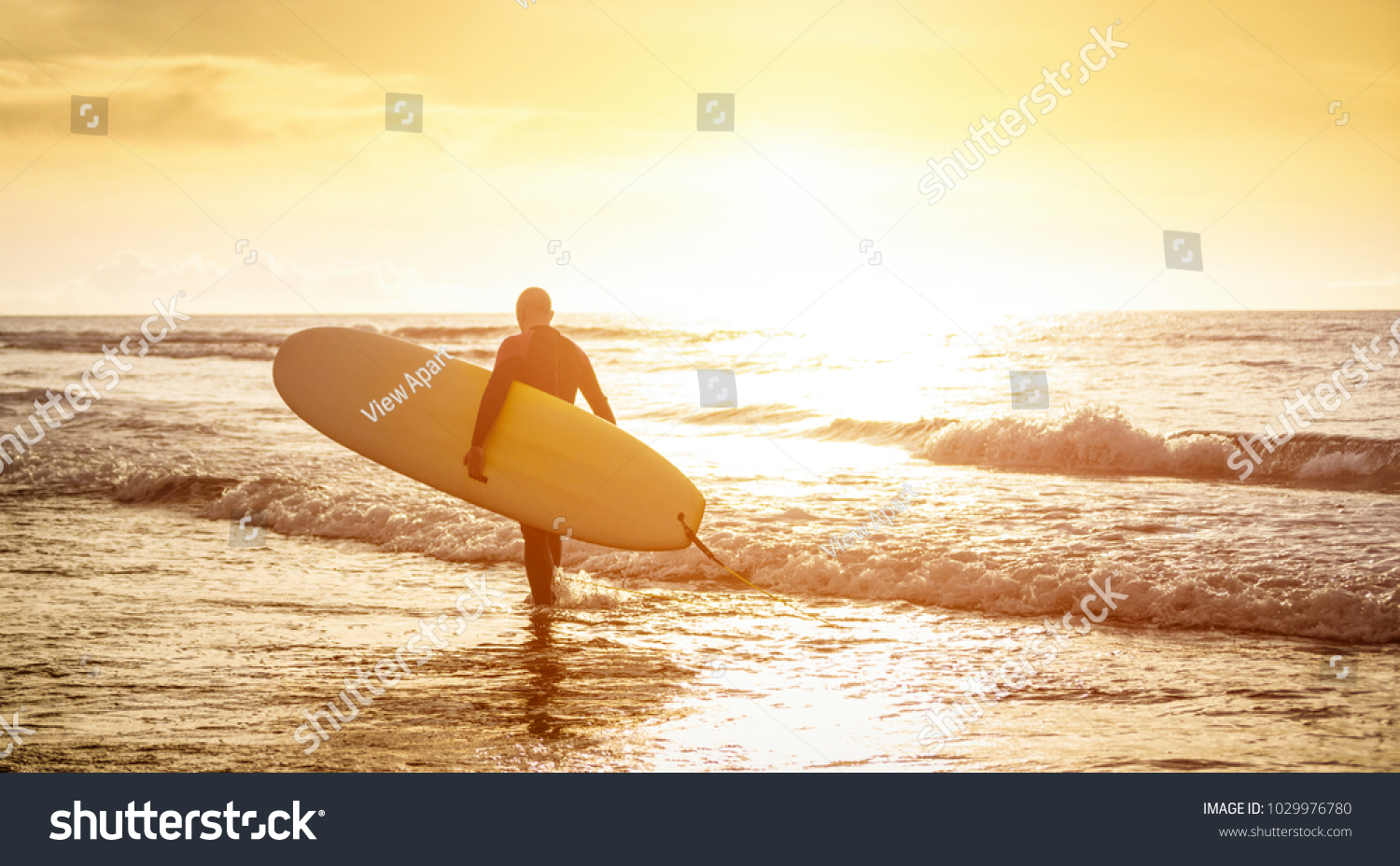 Guy surfer walking with surfboard at sunset in Tenerife - Surf long board training practitioner in action - Sport travel concept with sof focus water near feet - Warm sunshine color foltered tones