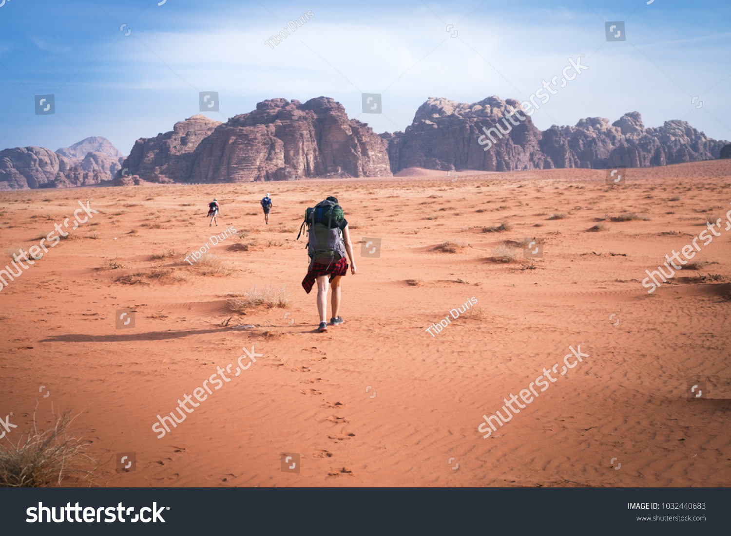 Two hikers in a sand desert. Tourist friends in Jordan natural park Wadi Rum.Group of backpackers walking on the road. Natural background.