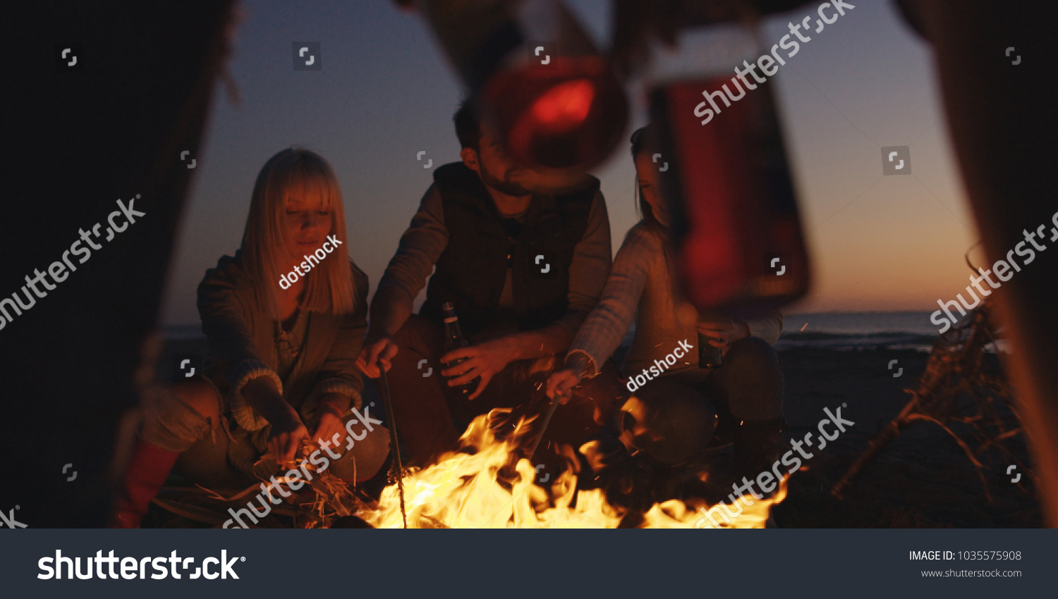 Group of young people having fun at beach around bonfire on sunset