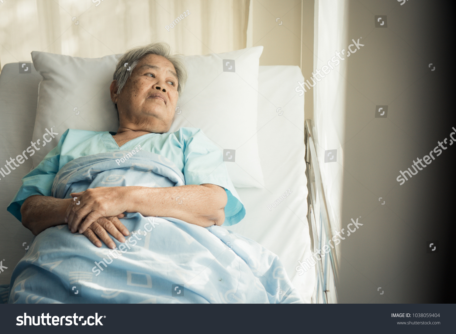 lonely asian elderly female patient lying on the bed in the hospital and looking away outside the window waiting to see her child and her family to visit.