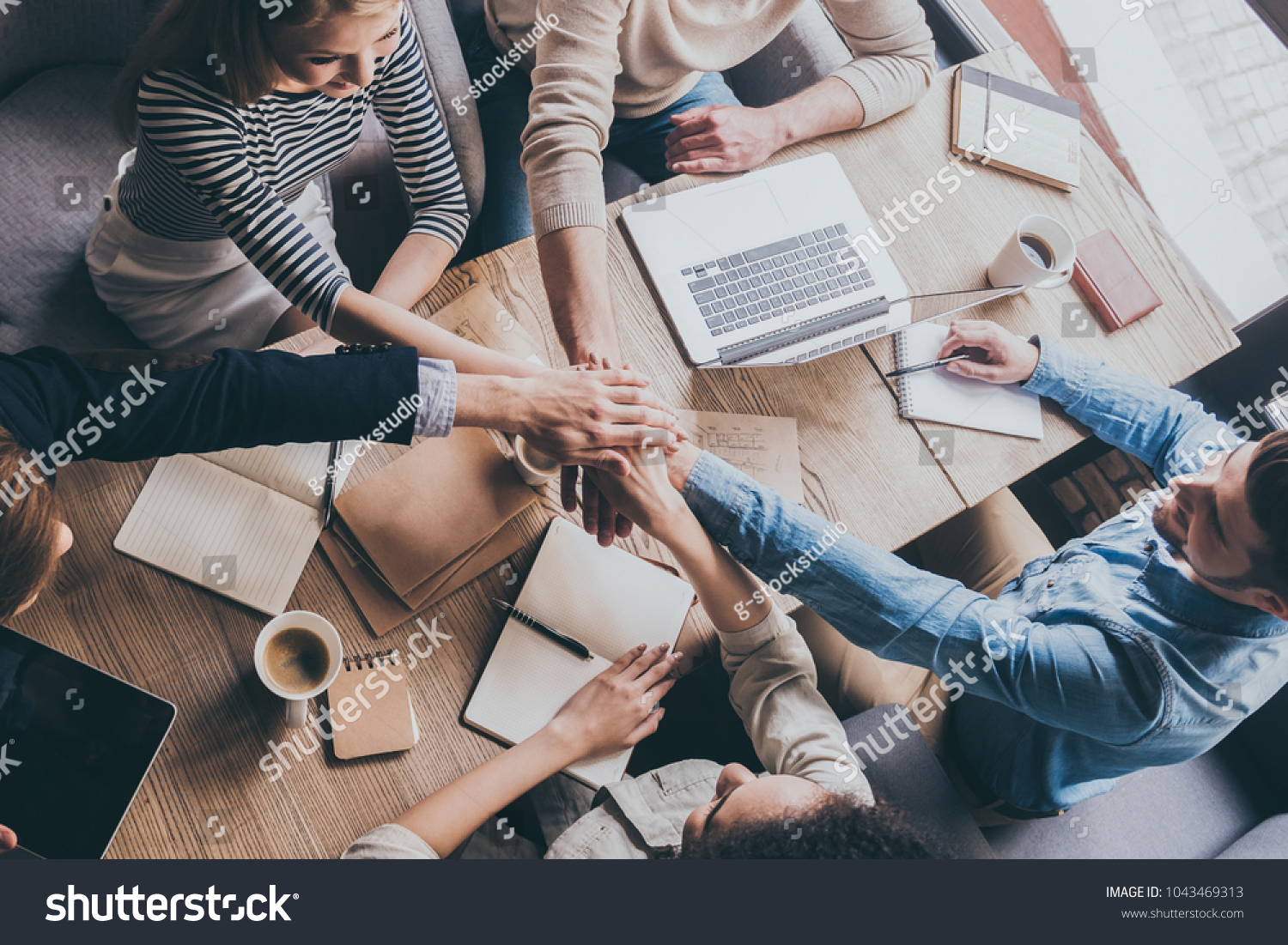 Successful team. Top view of young business people holding hands together while sitting at the office table together
