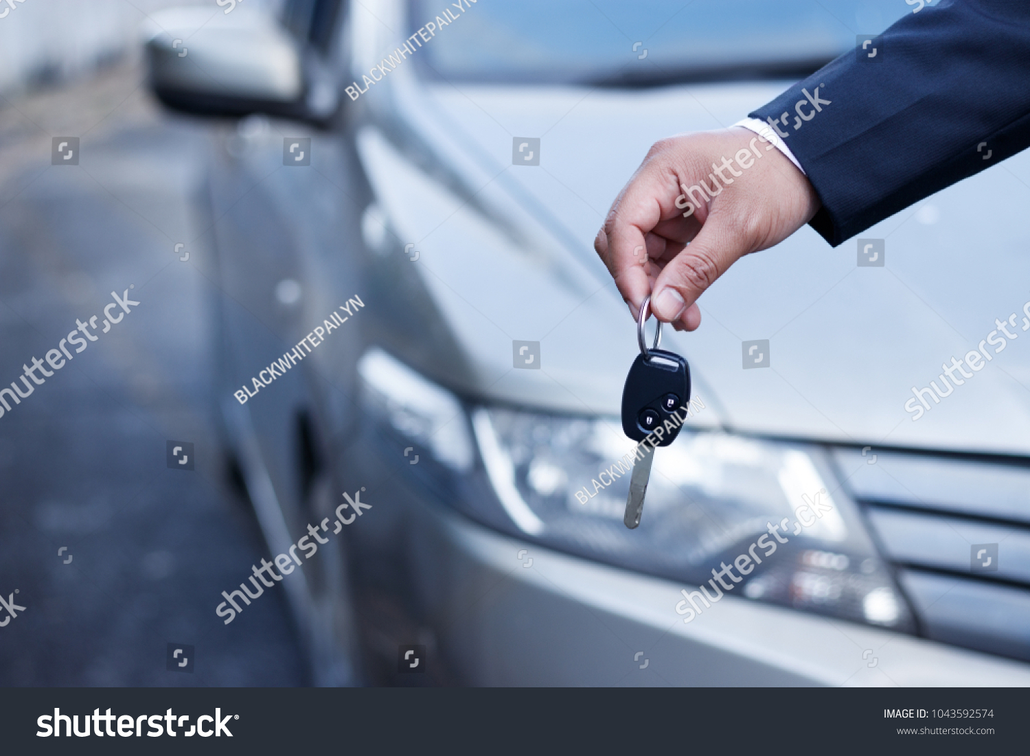 Business man holding car keys with car on background.