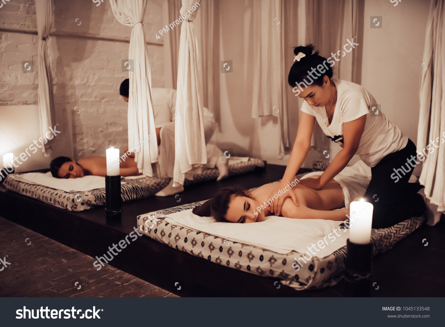Two young women are relaxing in spa and wellness center while receiving body massage. Beauty treatment concept.