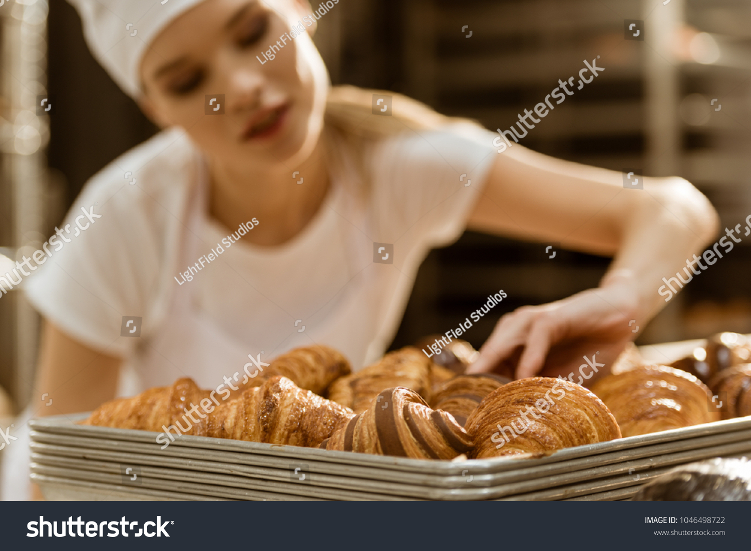close-up shot of young female baker doing examination of freshly baked croissants on baking manufacture