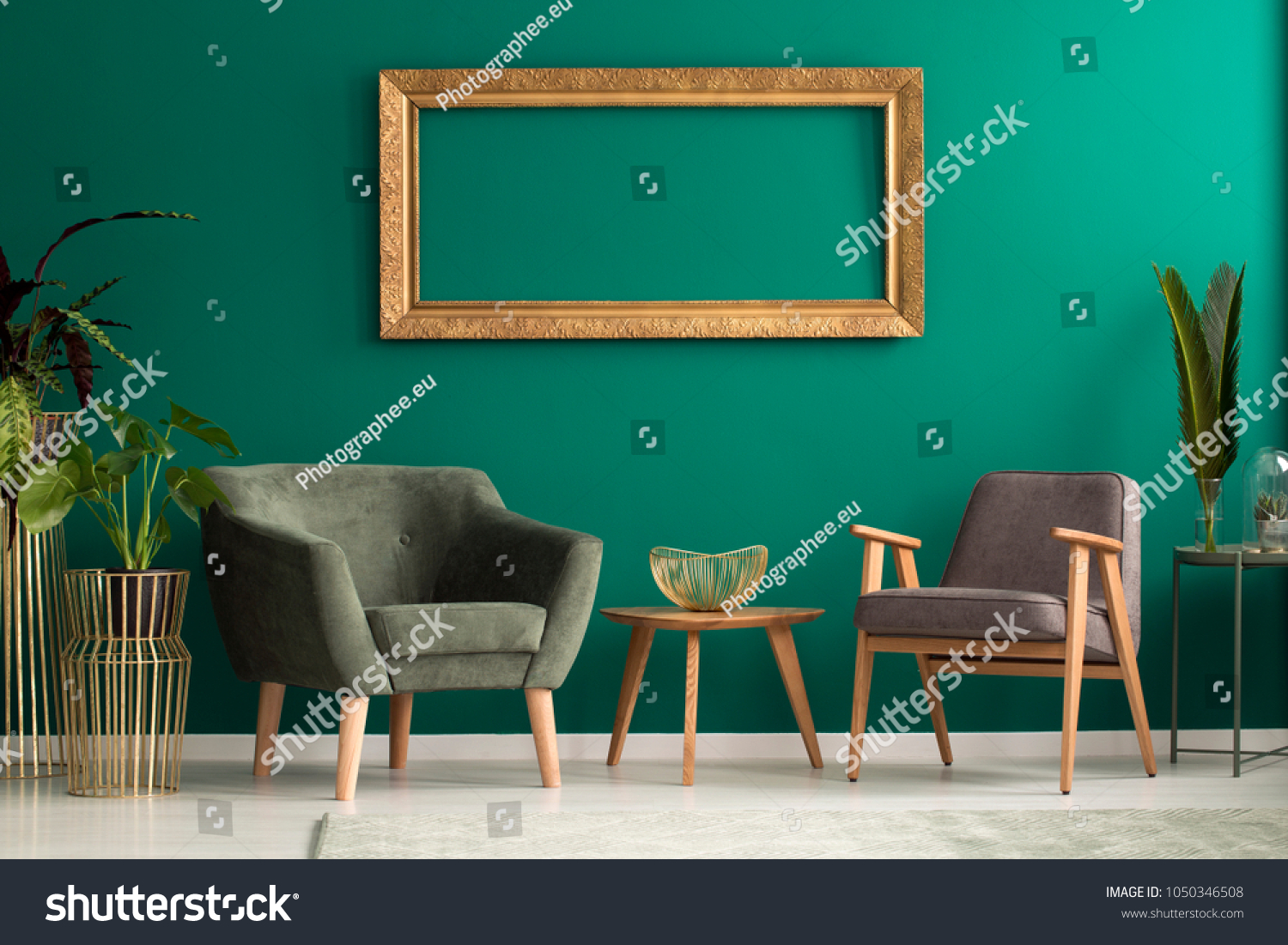 Elegant fruit bowl on a wooden table between retro armchairs with wooden legs in a luxurious green living room interior with plants