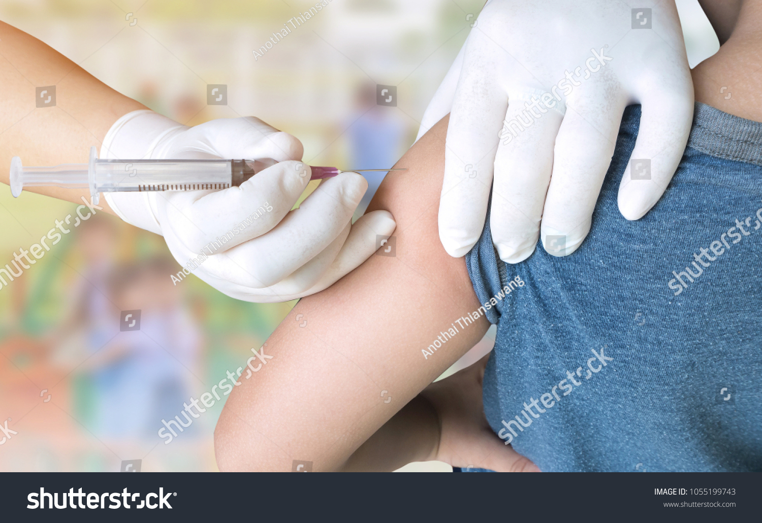 Doctor woman giving a child injection in arm on burred student playing with toy on playground in the school.