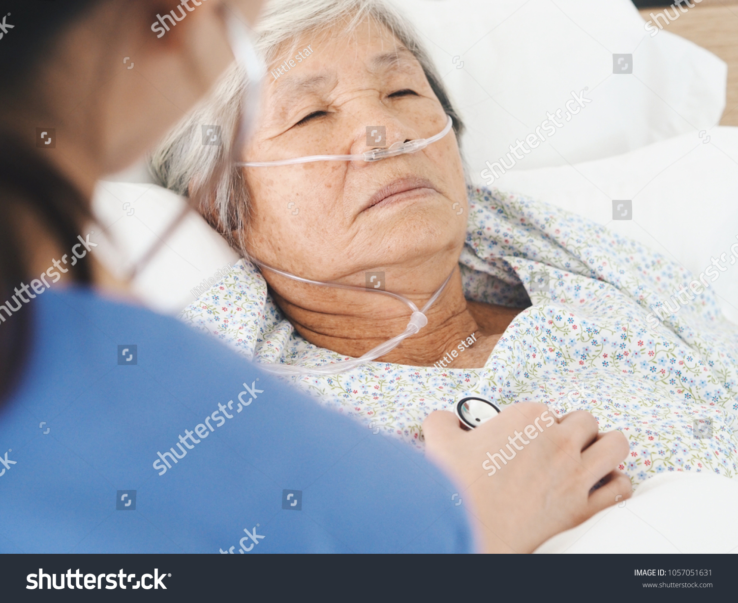 Elderly Asian woman laying on bed in hospital room.