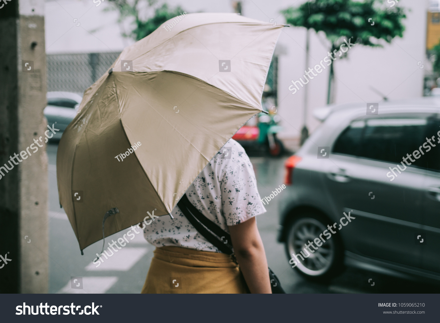 The girl is walking  holding an umbrella across the street in the rain.