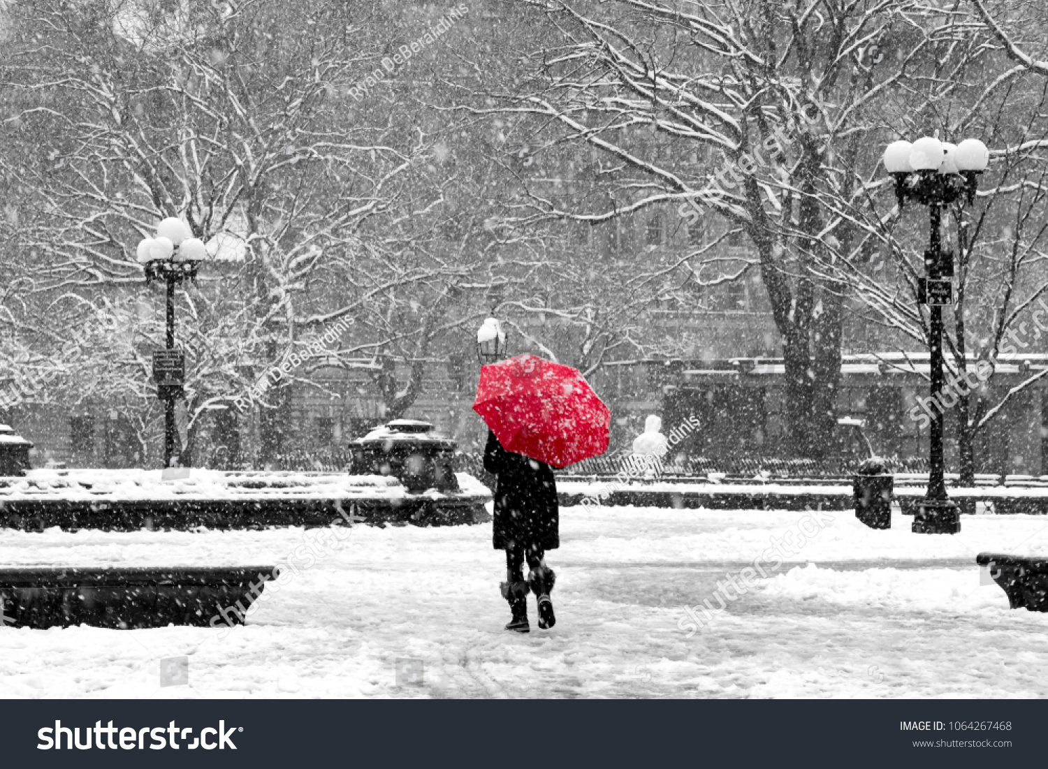 Woman with red umbrella walking through black and white landscape during nor’easter snow storm in Washington Square Park New York City