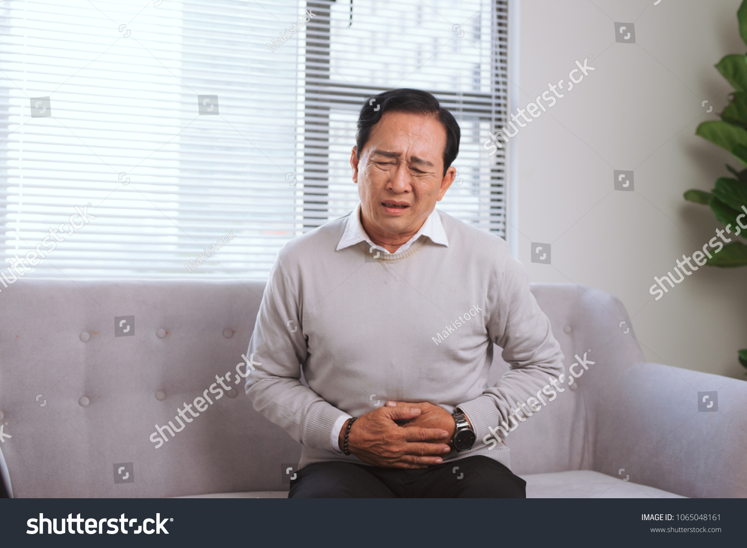Senior asian man with stomach ache while sitting on sofa
