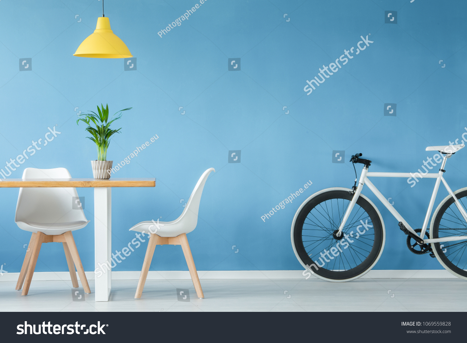 Minimal  modern interior with two chairs  a bicycle  a table with a plant on it and a yellow lamp above  against blue wall