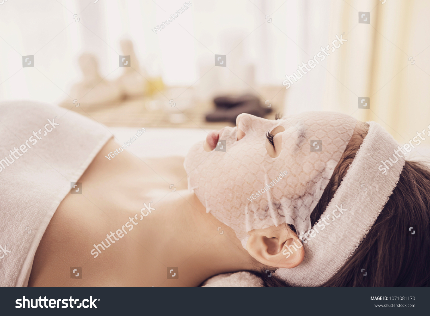 Spa therapy for young asian woman receiving facial mask at beauty salon.