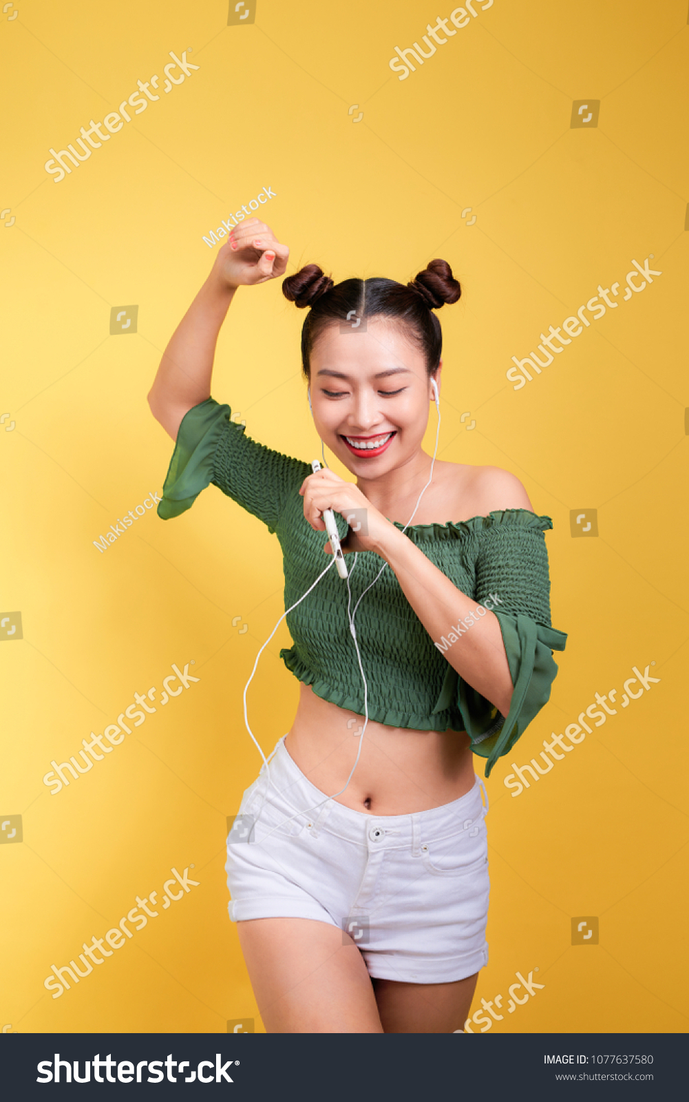 Fashion smiling asian woman listening to music in earphones  over yellow background